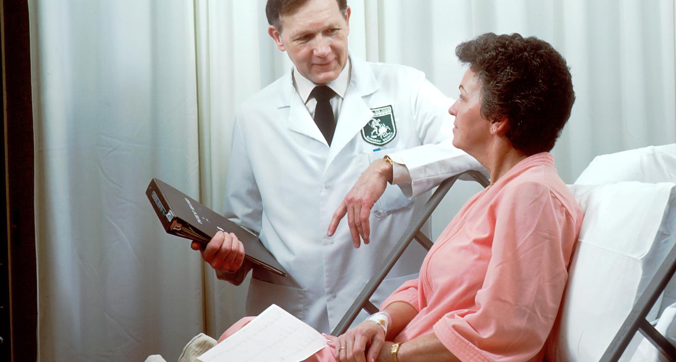 Man in a lab coat attending a patient holding a tablet.