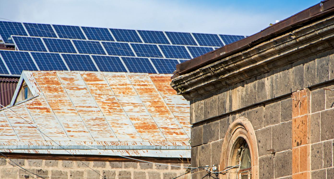 The image shows a contrast between a new solar panel on the building roof and an old houses roofs in Gyumri, Armenia