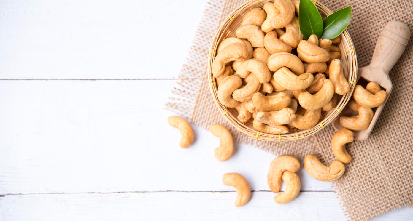 Cashew nuts with green leaves in basket and spoon isolated on white wooden background, selective focus, Healthy food