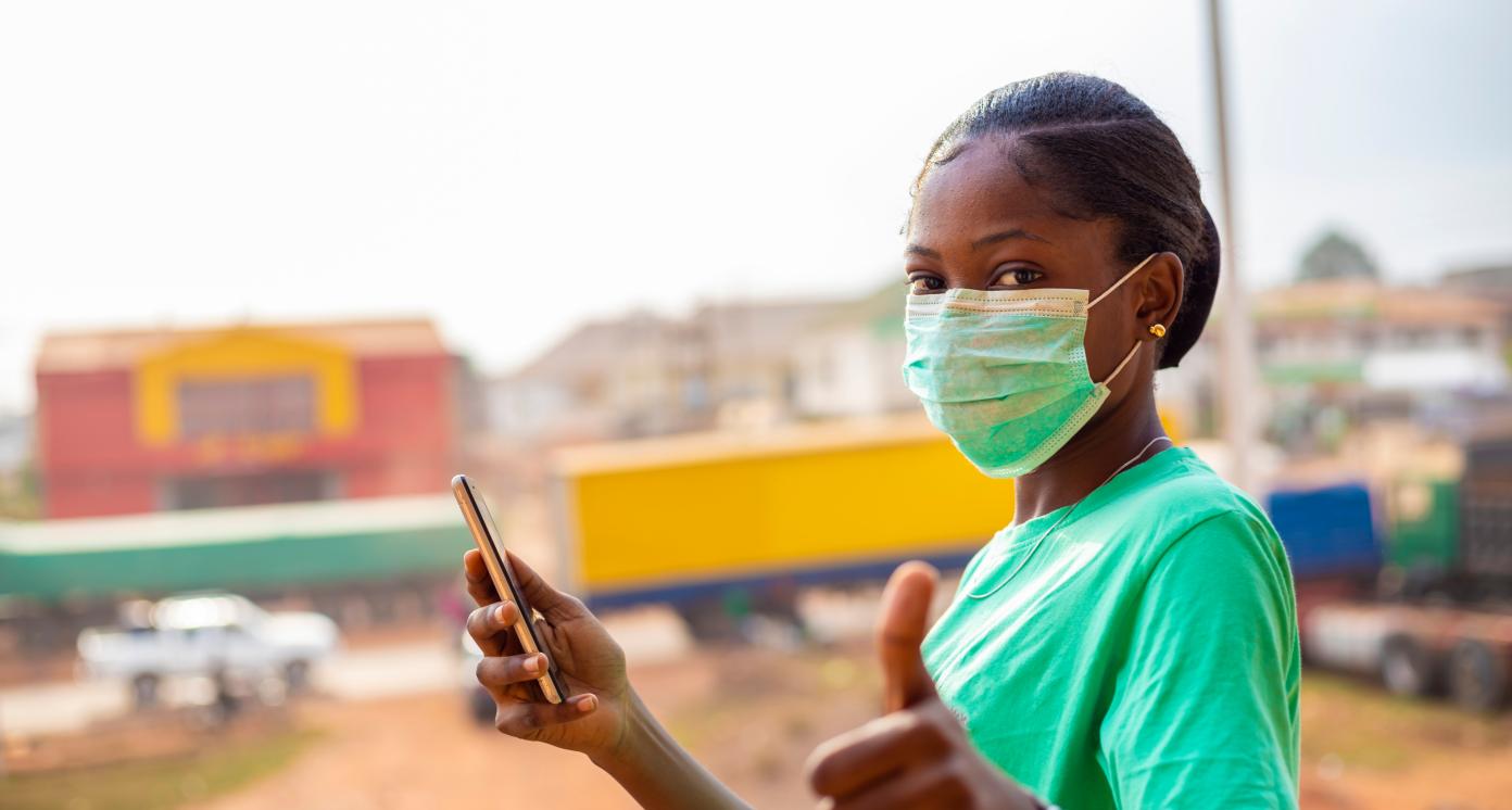 young black African woman doing a thumps up sign holding mobile phone