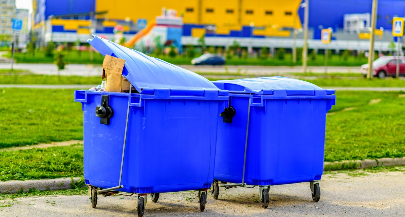 Two blue overfilled waste bins on wheels for collecting recyclable materials. Pollution and waste disposal. The concept of an ecologically clean environment, garbage recycling.