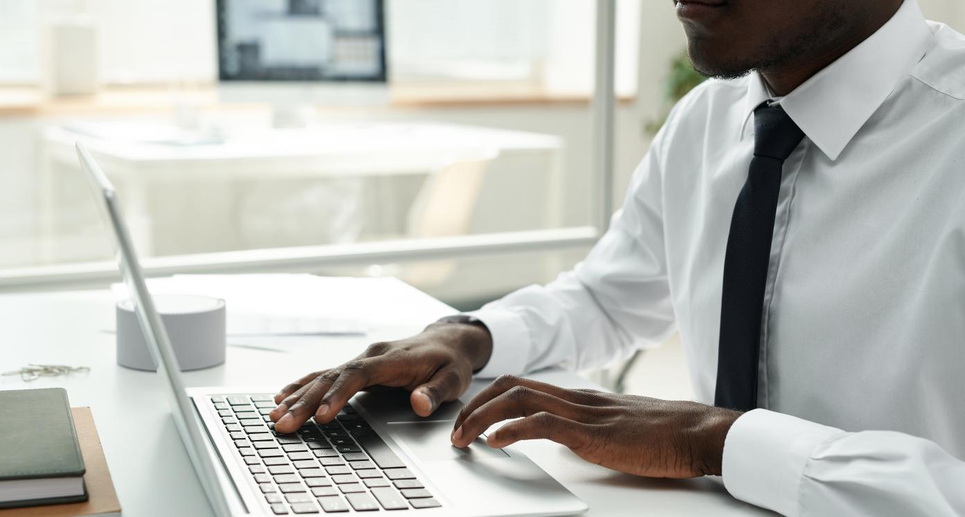 Close-up of African American businessman in white shirt working online on laptop at office