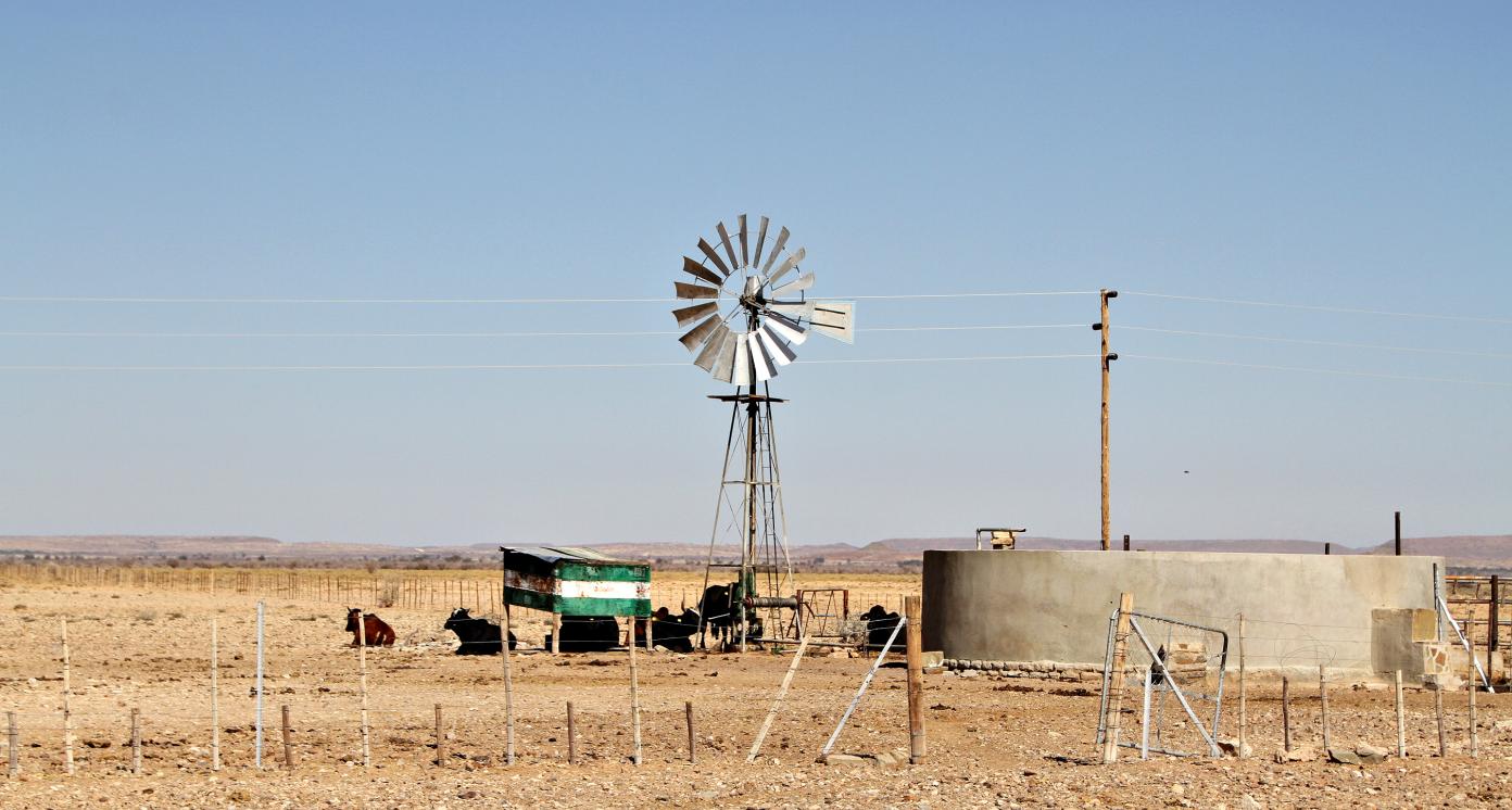 A windmill and water reservoir stand in a remote and desolate landscape on a rural farm in Namibia.