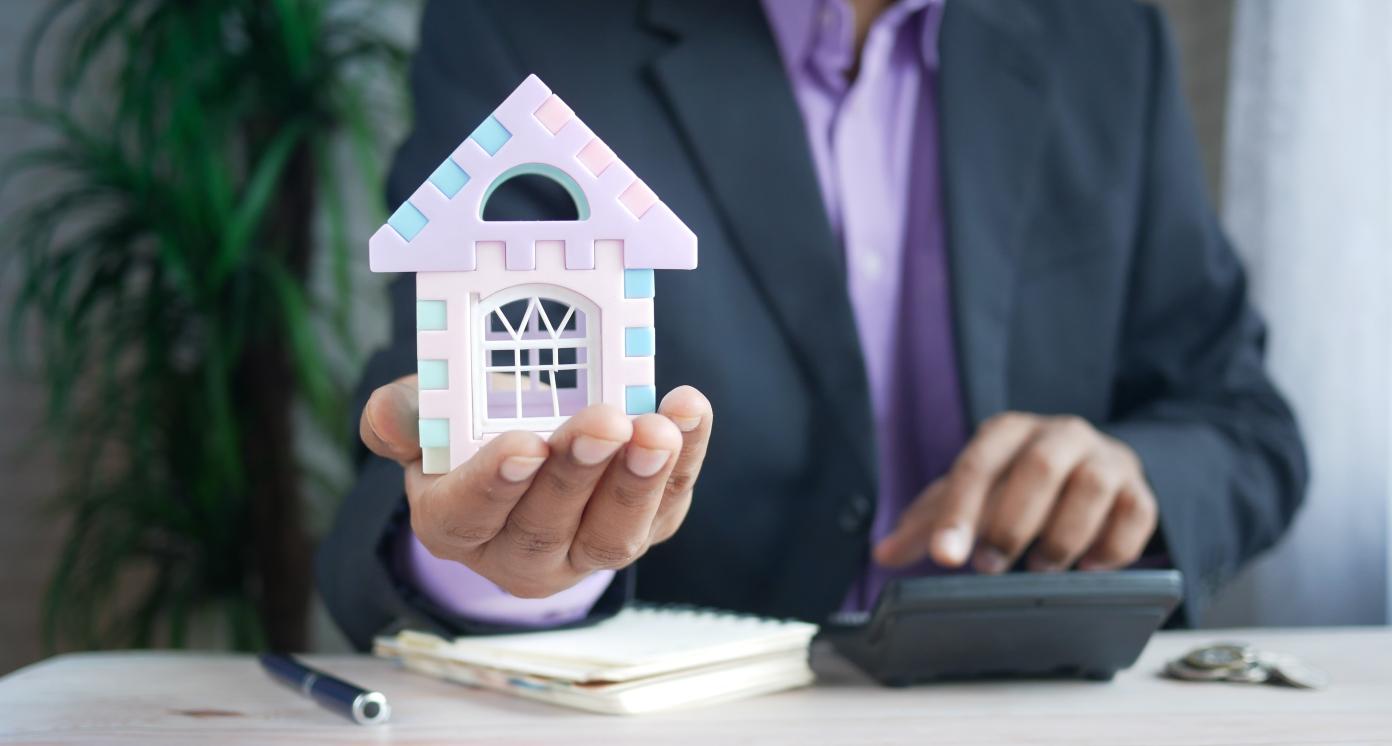 Man in a suit holding a miniature house