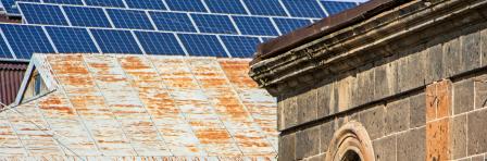 The image shows a contrast between a new solar panel on the building roof and an old houses roofs in Gyumri, Armenia