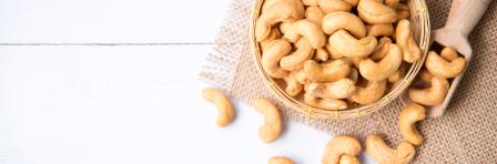 Cashew nuts with green leaves in basket and spoon isolated on white wooden background, selective focus, Healthy food