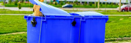 Two blue overfilled waste bins on wheels for collecting recyclable materials. Pollution and waste disposal. The concept of an ecologically clean environment, garbage recycling.