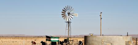 A windmill and water reservoir stand in a remote and desolate landscape on a rural farm in Namibia.